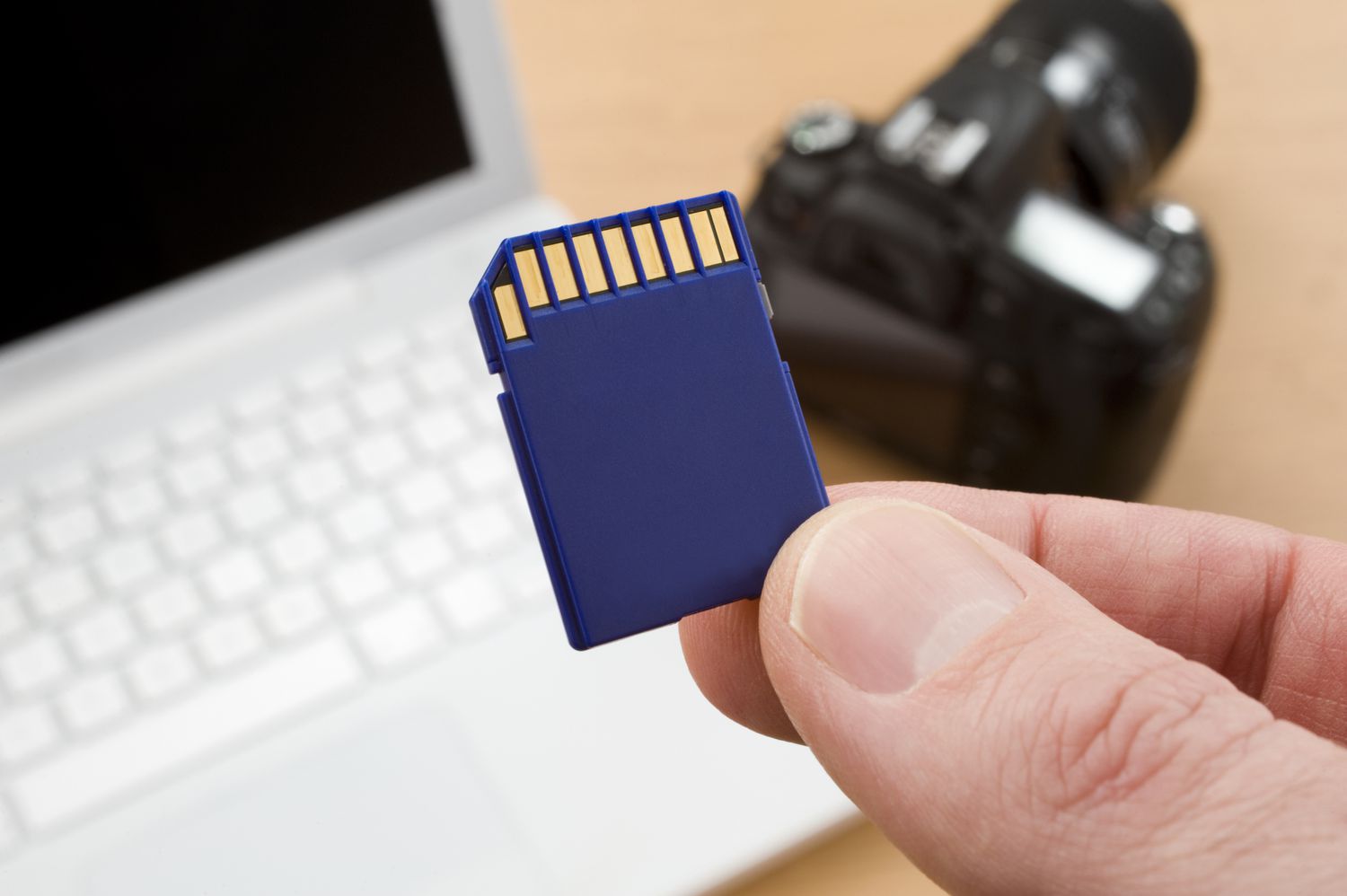 Close up of SD card with computer and camera in background